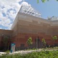 a large brick building against a blue sky with glasshouses on its roof